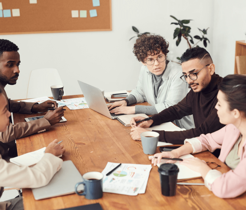 Five business professionals discussing work-related tasks in a modern meeting room.